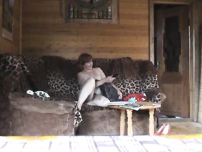 Полностью голая женщина в возрасте смотрит телевизор сидя на леопардовом диване